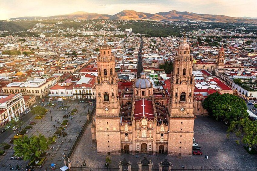 Una gran catedral con dos torres, rodeada por un paisaje urbano con edificios y una cadena montañosa al fondo. 2