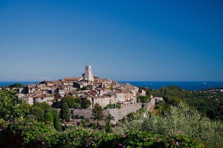 A coastal town with historic buildings, a prominent church tower, and a clear view of the sea. 1