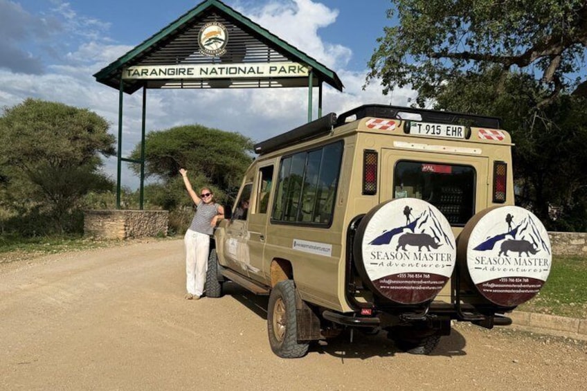 A safari vehicle with 'Season Master Adventures' branding parked at Tarangire National Park entrance. 1