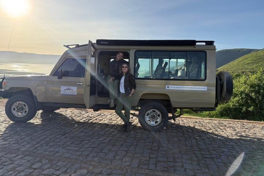 A safari vehicle parked on a cobblestone path with a person standing in front. 2