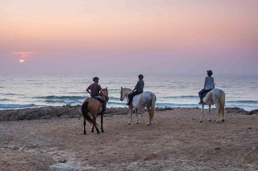 Three people riding horses on a beach at sunset. 2