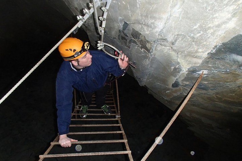 A person climbing a metal ladder in a cave with a helmet and harness. 2
