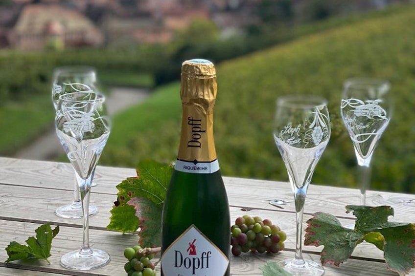 A bottle of Doeff wine, two glasses, and grapes on a wooden table with a vineyard in the background. 5
