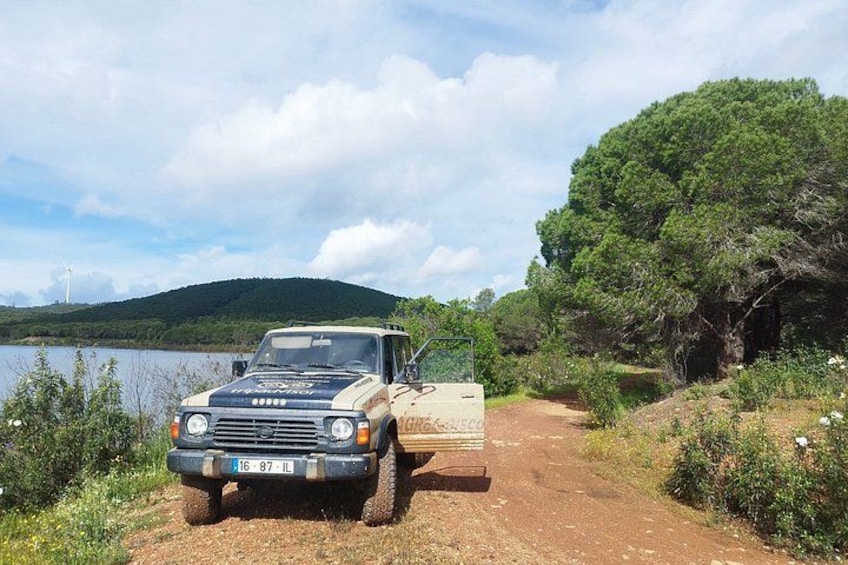 Un vehículo estacionado en un camino de tierra junto a un lago, con árboles y colinas al fondo. 5