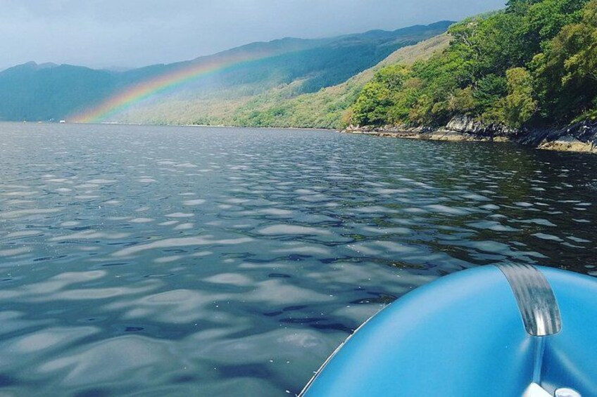 A body of water with a rainbow, a boat, and a forested hillside. 2