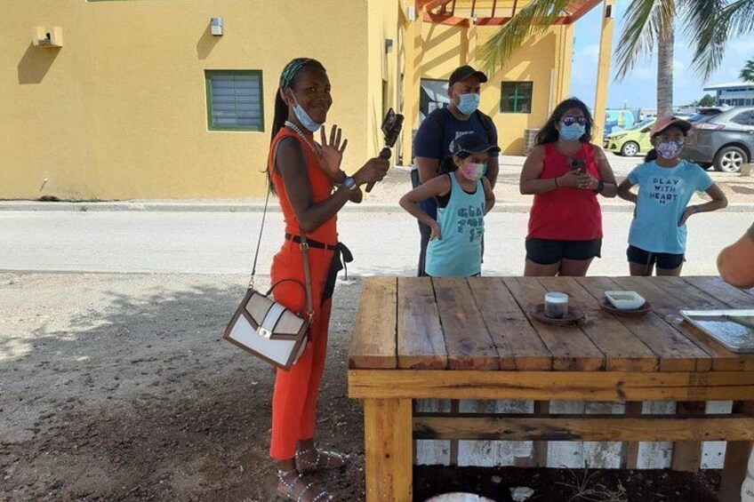 Un grupo de personas de pie al aire libre cerca de una mesa de madera con comida. 1