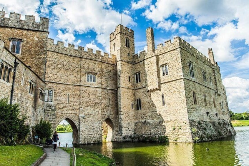 A historic stone castle with a moat, a pathway, and a clear sky. 1
