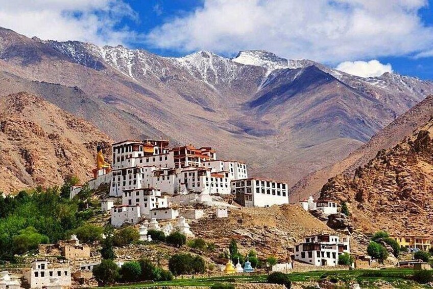 A monastery complex on a hillside with snow-capped mountains in the background. 2