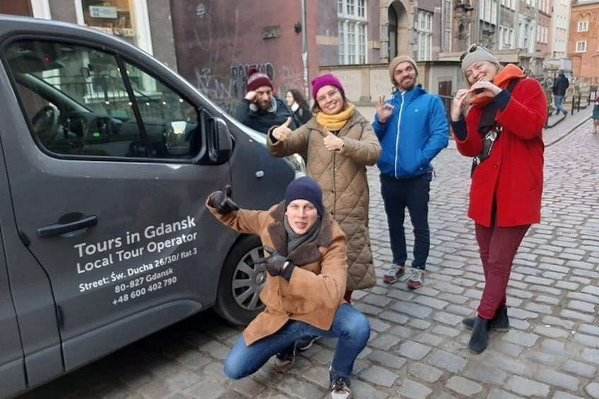 Un grupo de personas posando cerca de un autobús turístico con un cartel que dice 'Tours in Gdansk'. 4