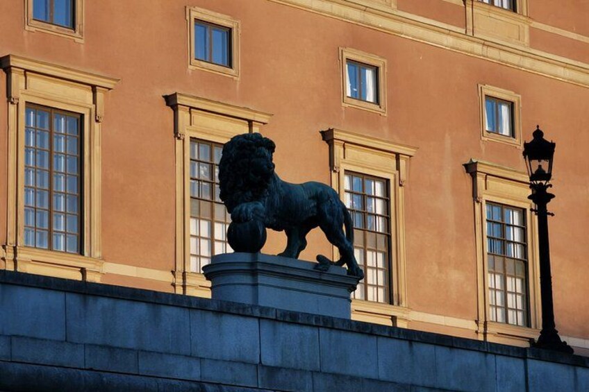 A lion statue on a pedestal in front of a building with large windows and a street lamp. 4