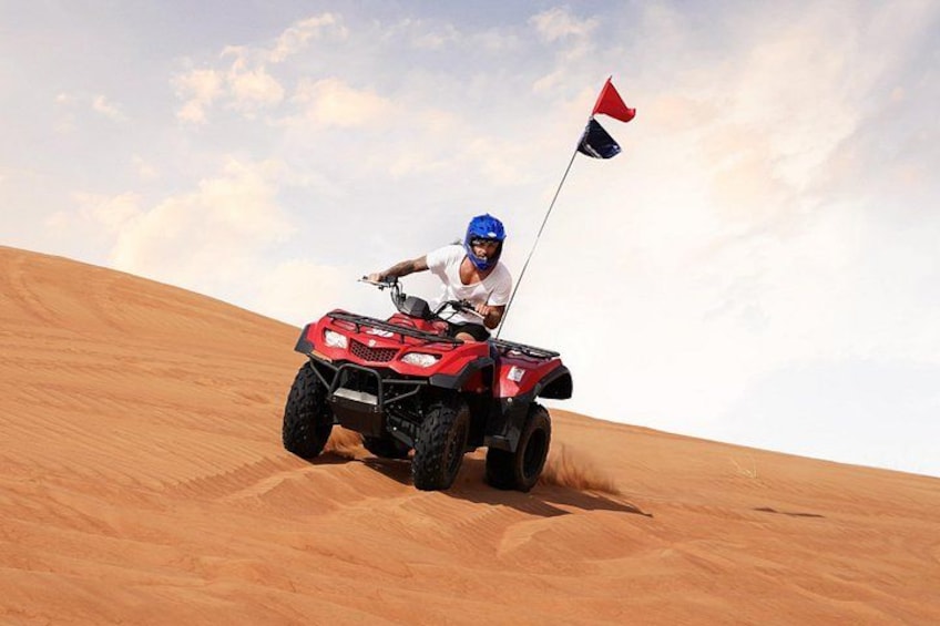 En person kører på en rød ATV op ad en sanddune med et flag. 3