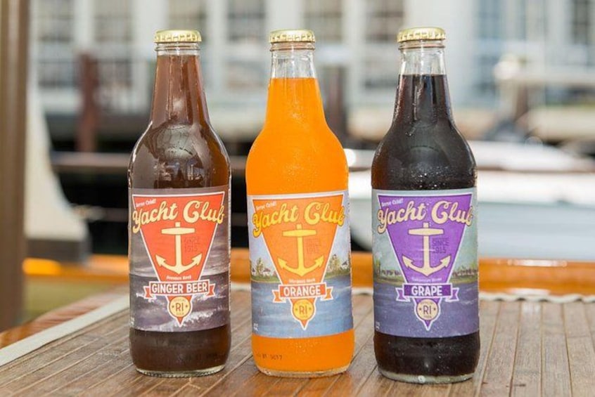 Three bottles of Yacht Club beverages on a wooden surface with a marina in the background. 2