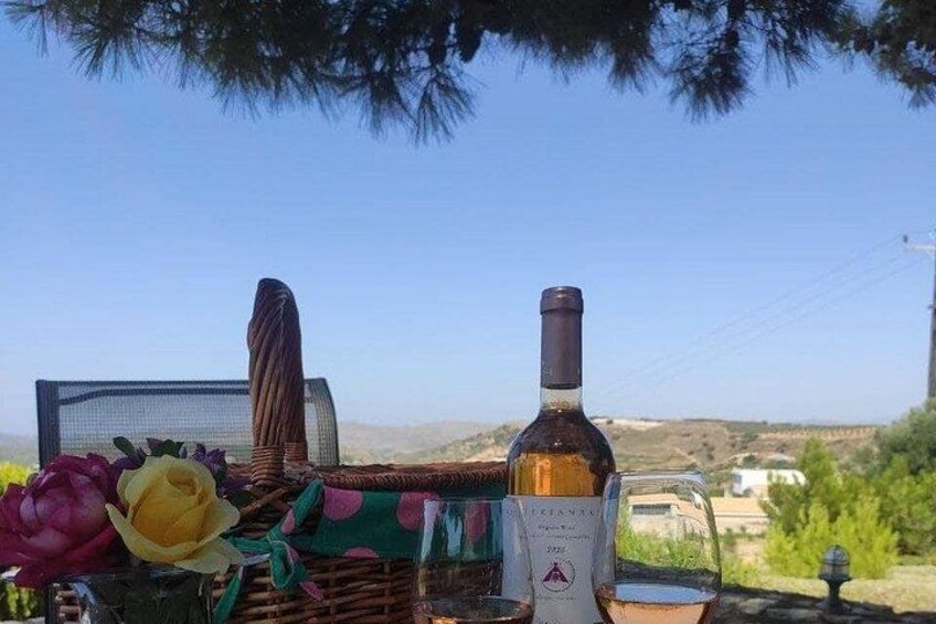 A bottle of wine, a glass, and a wicker basket with flowers on a table with a scenic view in the background. 3