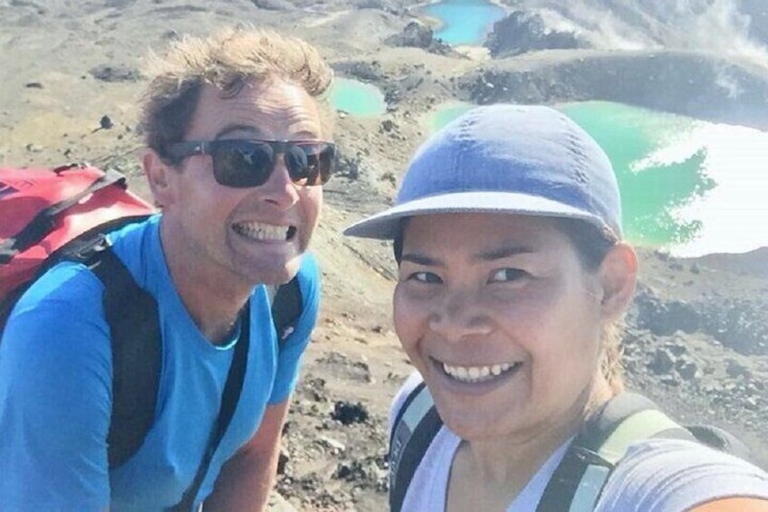 Two people taking a selfie on a beach with volcanic rocks and green pools in the background. 3
