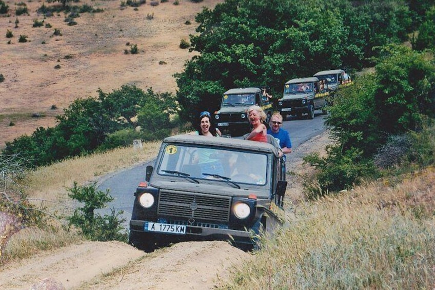 Eine Kolonne Geländewagen auf einer unbefestigten Straße, umgeben von Grün. 5