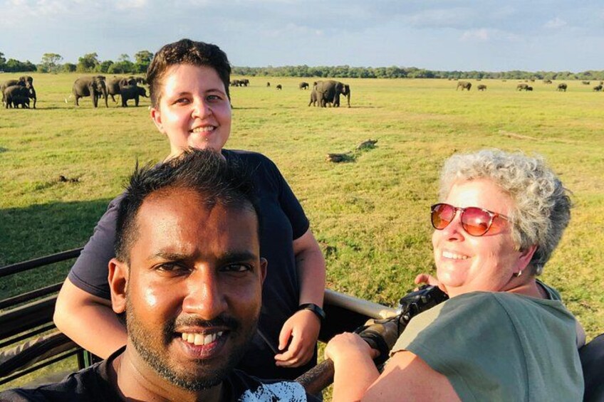 Ett safari-fordon med människor i förgrunden och elefanter i bakgrunden. 4
