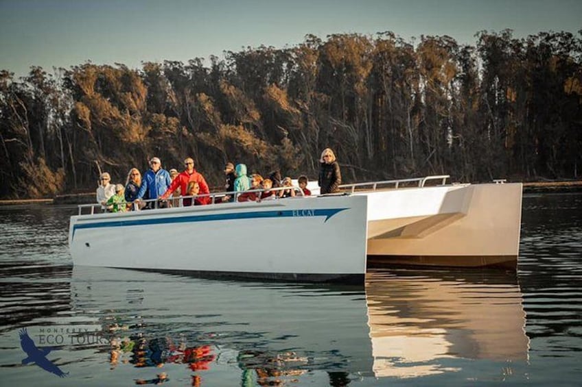 Un bote con gente a bordo, rodeado de agua tranquila y árboles al fondo. 1