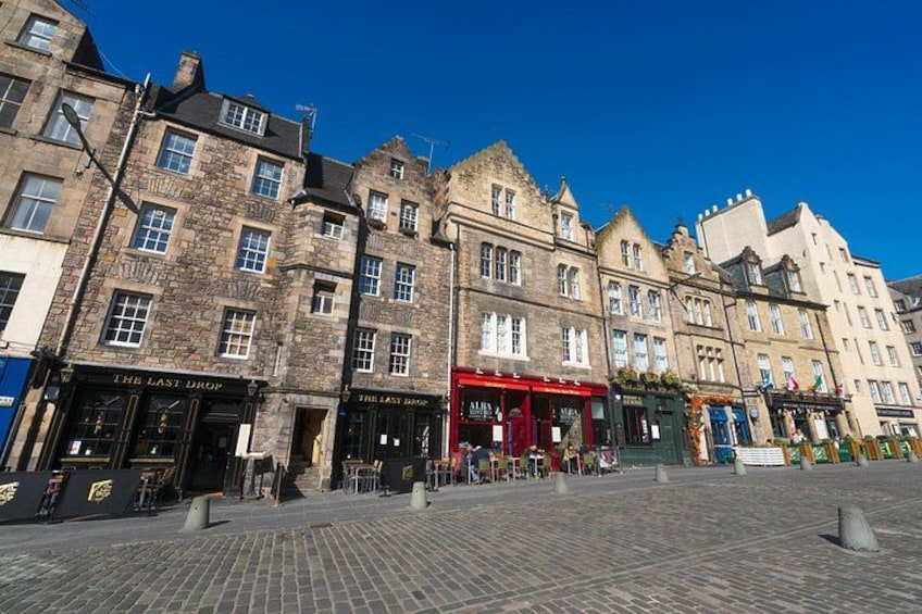 A historic street with cobblestone pavement, traditional architecture, and storefronts including 'The Last Drop' pub. 3