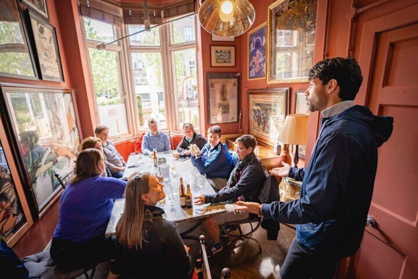 Eine Gruppe von Menschen sitzt an einem Tisch in einem Raum mit großen Fenstern und gerahmten Bildern an den Wänden. 1