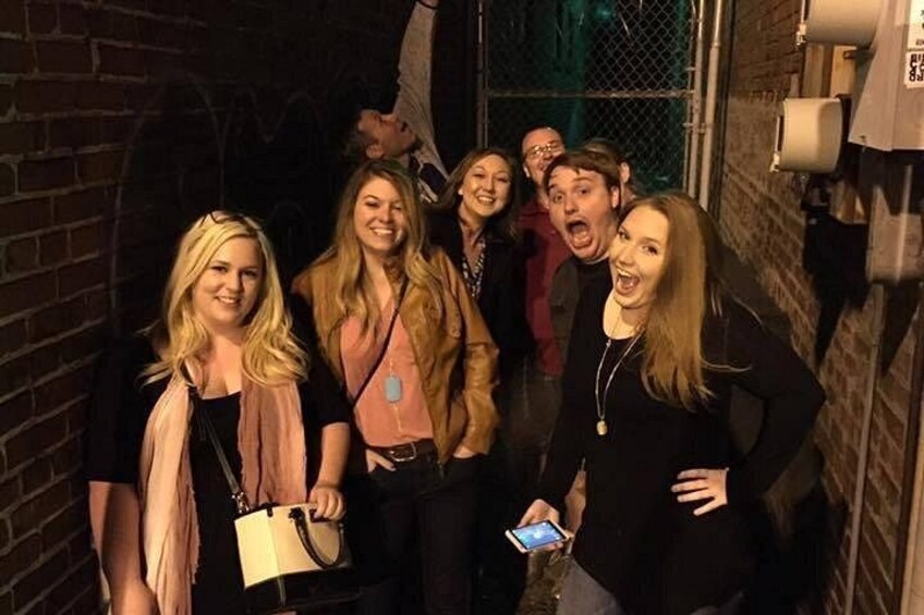 A group of people standing in a narrow alleyway with brick walls and a metal gate. 2