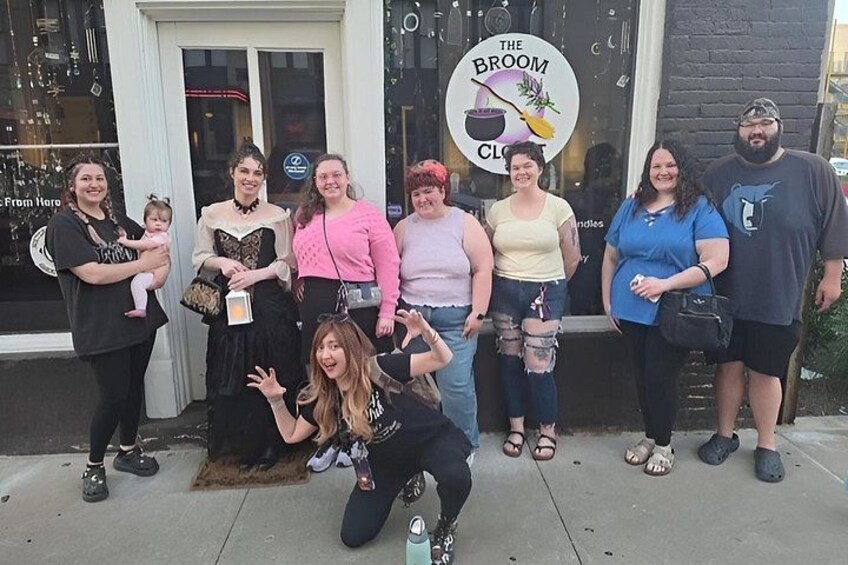 A group of people posing in front of a shop with a sign that reads 'The Broom Closet.' 4