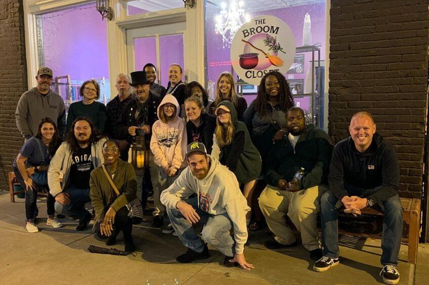 A group of people posing in front of a storefront with a sign that reads 'The Broom Closet.' 2