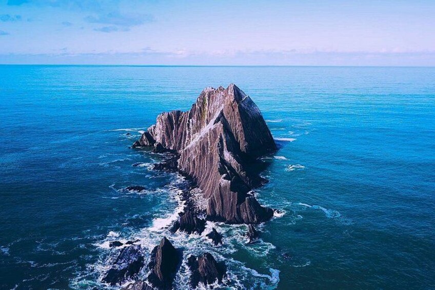A rocky island surrounded by blue ocean waves. 1