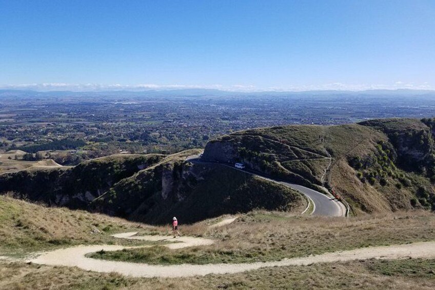 Una carretera serpenteante en una ladera con una persona de pie sobre un pequeño montículo. 4