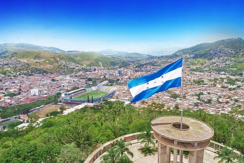 A cityscape with a flag on a tower, a stadium, and surrounding hills. 1