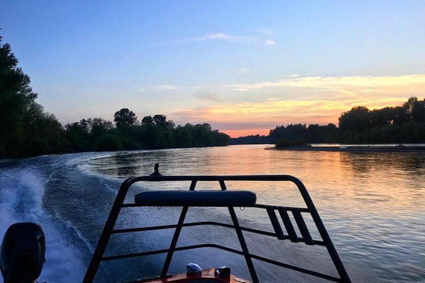 Une rivière où l’on voit un bateau en mouvement, entourée d’arbres et illuminée par le ciel au coucher du soleil. 1