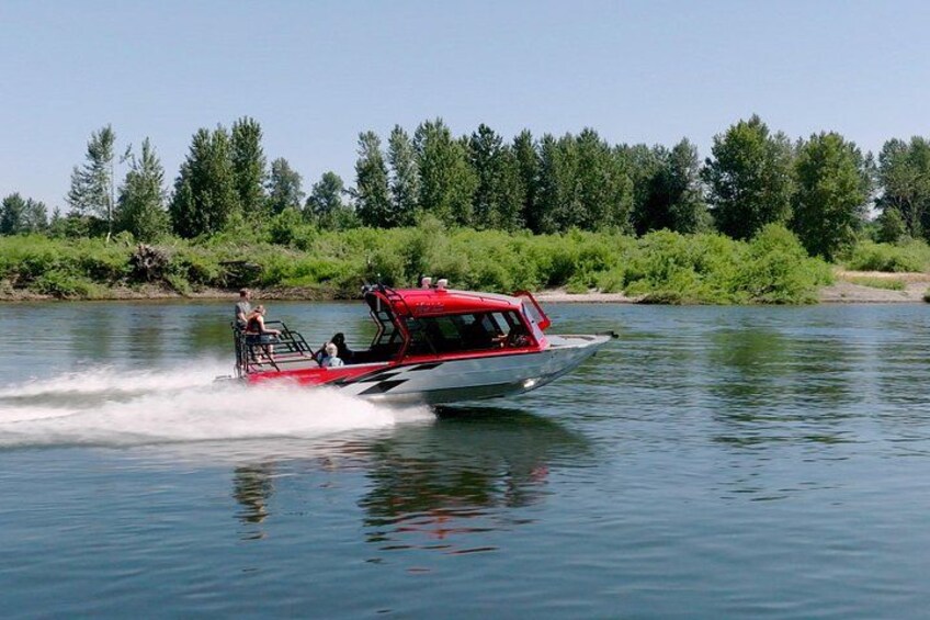 Un bateau rouge et blanc filant à toute vitesse sur une eau calme, transportant des passagers et entouré d’une rive bordée d’arbres. 5