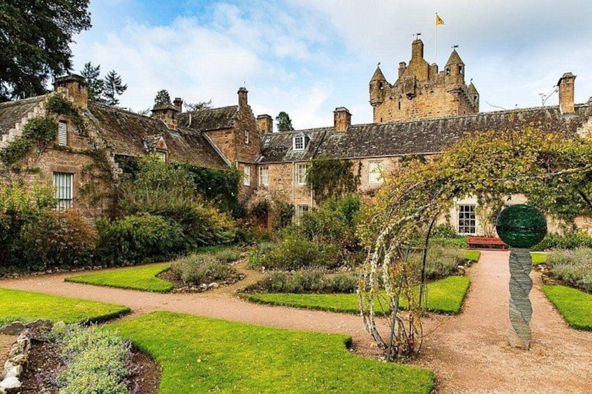 Ein historisches Steinhaus mit einem Gartenweg, der zu einer Burg führt. 1