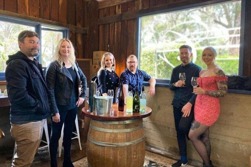 A group of people standing around a wooden barrel with bottles and glasses. 5