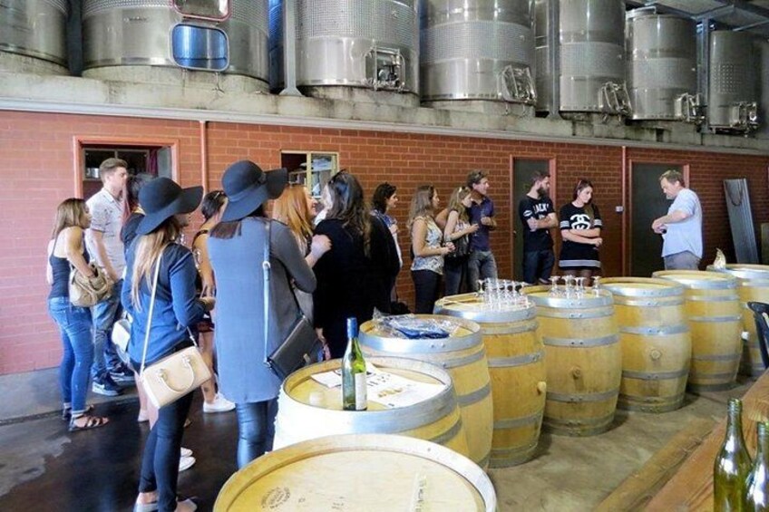 A group of people at a winery with large wine barrels and stainless steel tanks. 3
