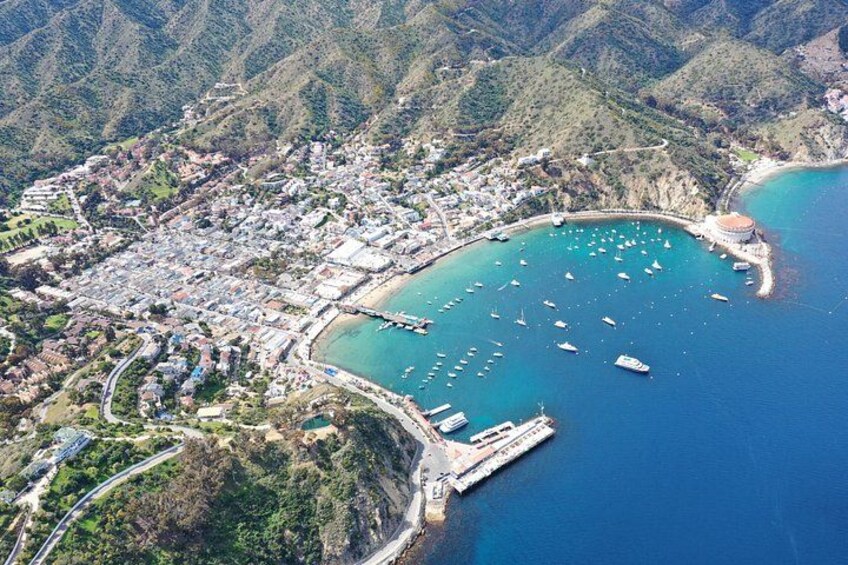 An aerial view of a coastal town with a marina, surrounded by hills and mountains. 3
