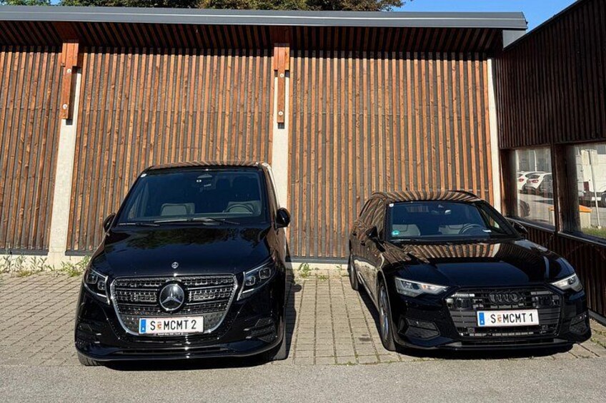 Two black Mercedes-Benz cars parked in front of a wooden building with a metal roof. 2
