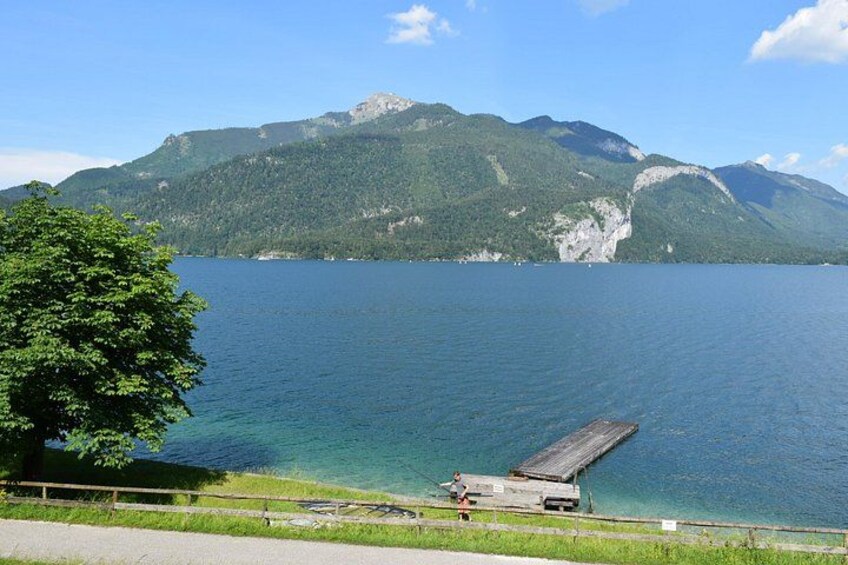 A lake with a dock, a tree, and mountains in the background. 5