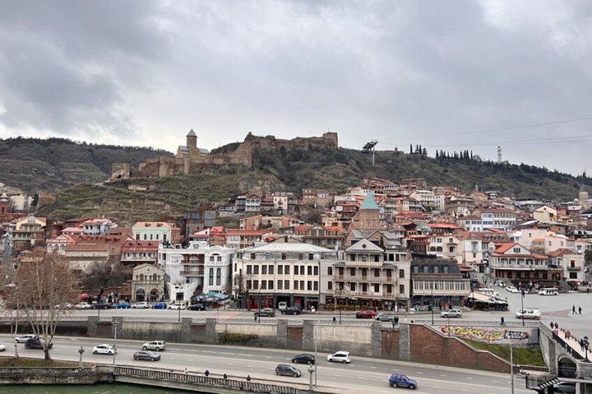 A cityscape with historic buildings, a prominent hilltop fortress, and a modern highway. 2