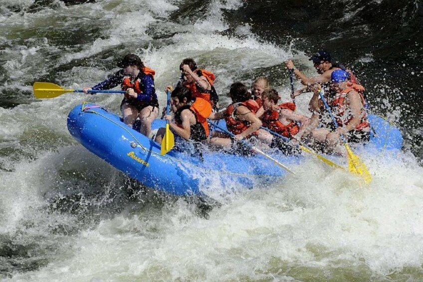 A group of people in a blue raft navigating through whitewater rapids. 3