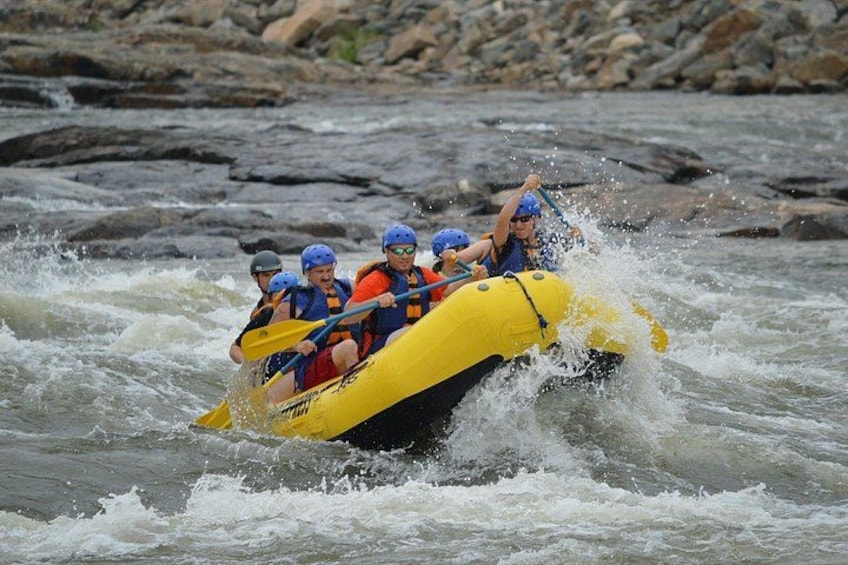 A group of people in a yellow raft navigating through a river with rapids. 2