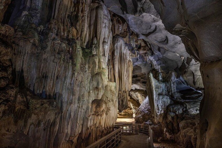 Una grotta con stalattiti e stalagmiti, un percorso in legno e un interno scarsamente illuminato. 3