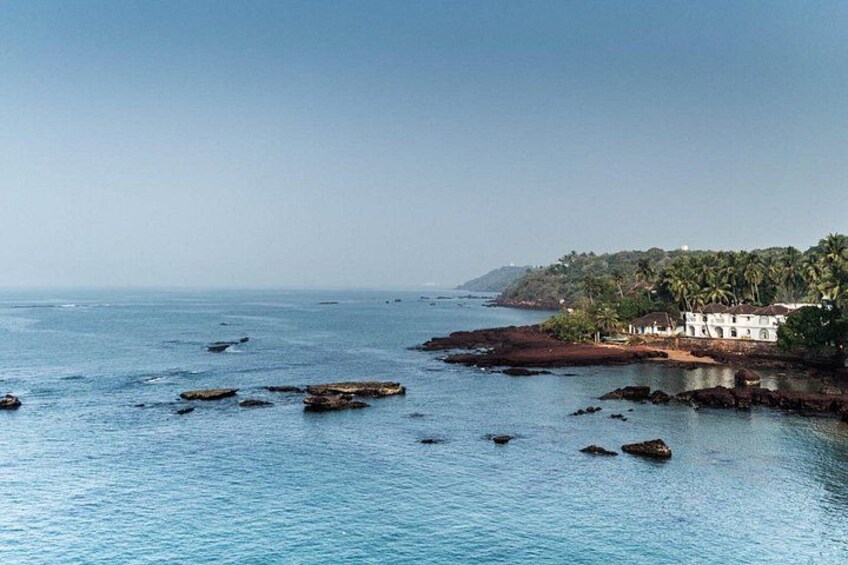 A coastal landscape with calm waters, scattered rocks, and a building with a red roof near the shore. 2