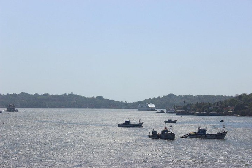 A calm body of water with several boats, a distant shoreline with trees, and a clear sky. 4