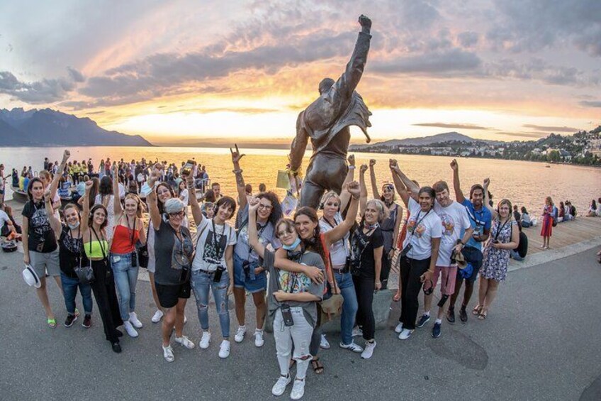 A group of people posing with a statue by a waterfront during sunset. 2