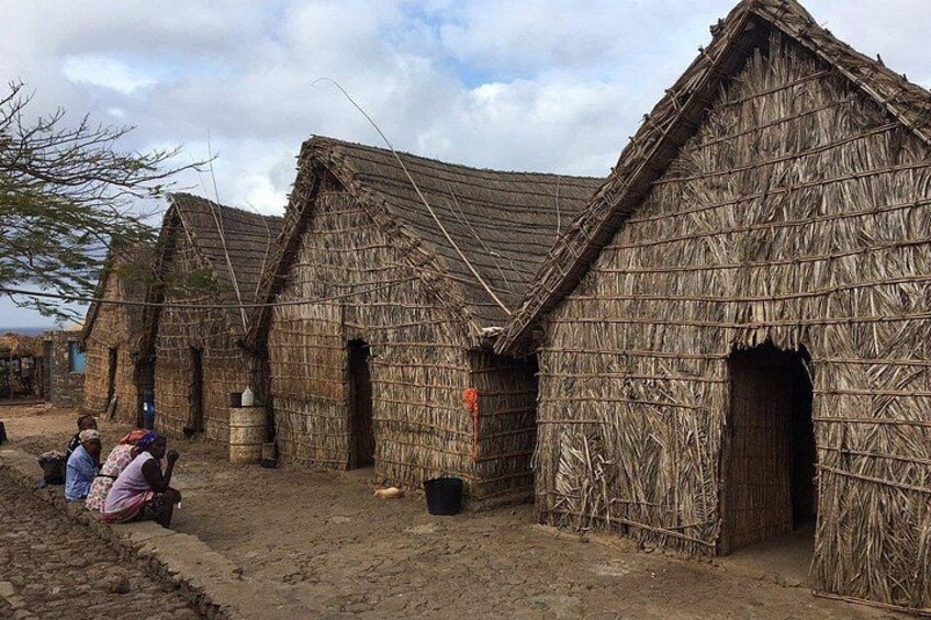 Traditional thatched-roof huts, a dirt ground, and a few people in the foreground. 1