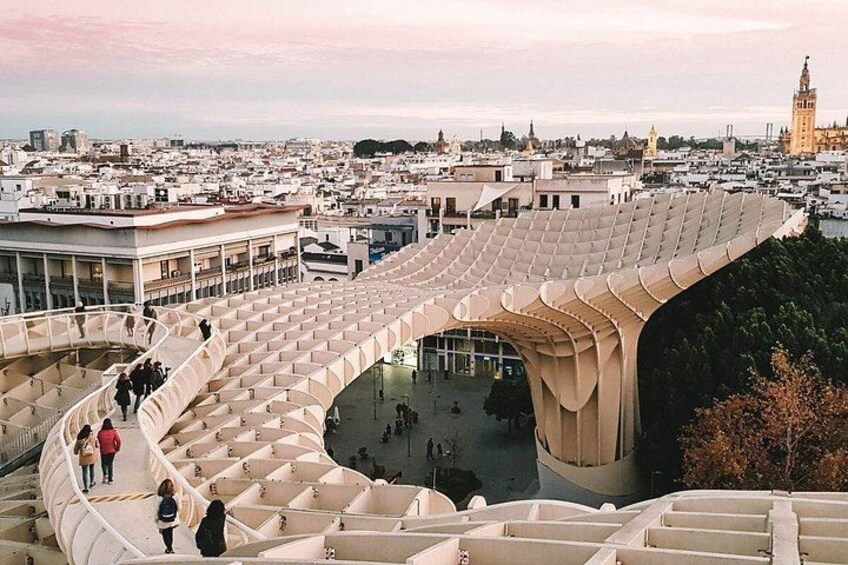 Une vaste structure architecturale moderne, dotée d’un toit incurvé, qui s’élève au milieu d’un paysage urbain composé de différents bâtiments et où l’on aperçoit, au loin, une tour imposante. 4
