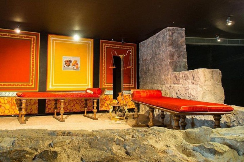 Une exposition dans un musée comprenant un banc rouge, un mur de pierre et des tableaux encadrés. 4