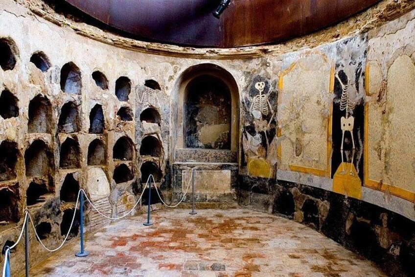 Une pièce circulaire antique, dotée de niches en arc de cercle, d’une porte centrale et de squelettes peints sur les murs. 5
