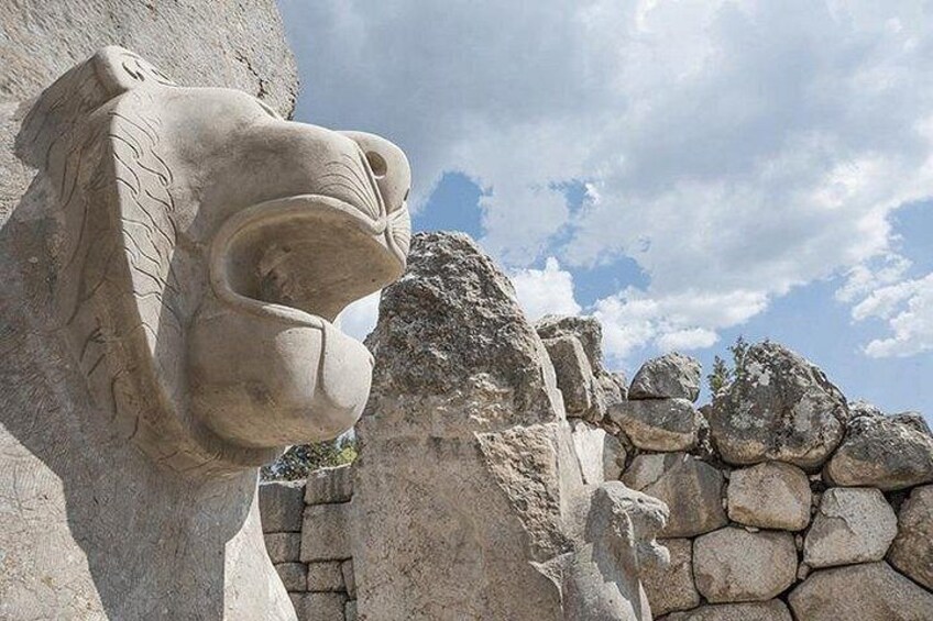 A large stone lion head sculpture with a rugged stone wall in the background. 3