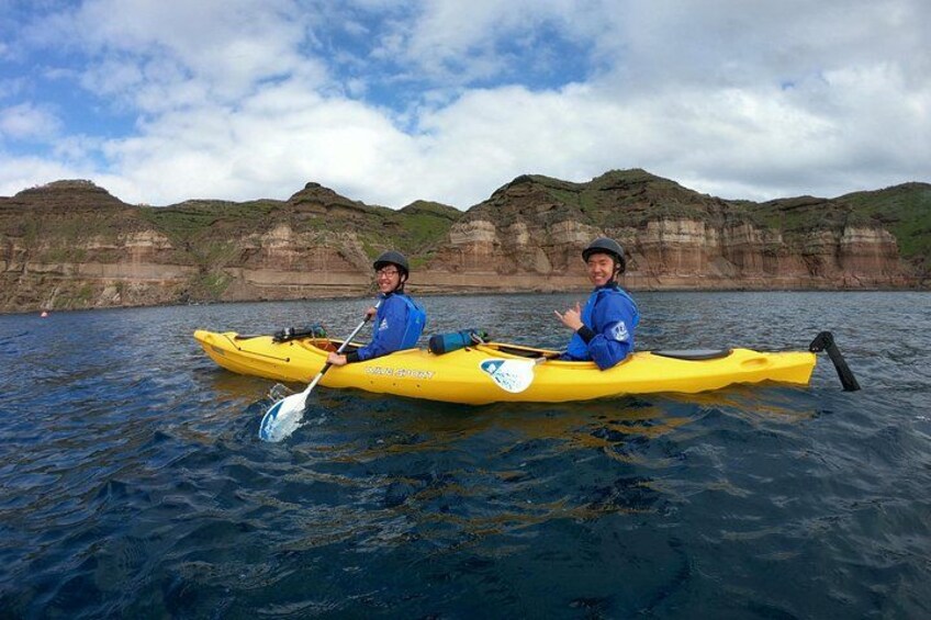 Two people kayaking on a body of water with cliffs in the background. 2